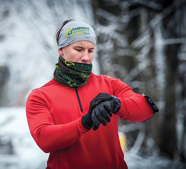 Runner wearing warm clothes looking at sport watch during winter gaiter sleeves